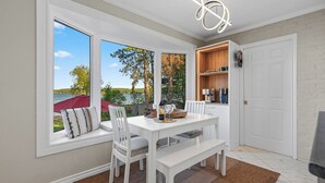 A dining area with a white table, chairs, and a view of the outdoors. - Stylish Sandy Beach 4-Bed Waterfront (Tiny)