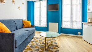 Una sala de estar moderna con un sofá azul, una mesita de centro de vidrio y un tapete estampado.