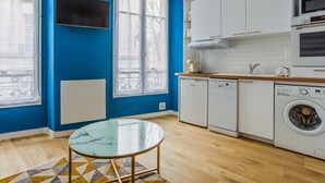 Una cocina moderna con armarios blancos, horno empotrado, microondas y lavavajillas. Hay una mesa de vidrio con un tapete de diseño geométrico.