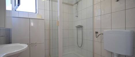 Een badkamer met douche, toilet en wastafel.