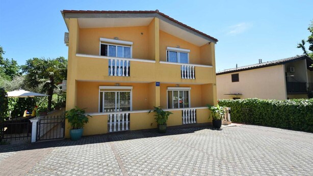 A two-story building with balconies, a paved courtyard, and potted plants.
