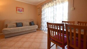 A living room with a sofa, a dining table with chairs, and a window with curtains.