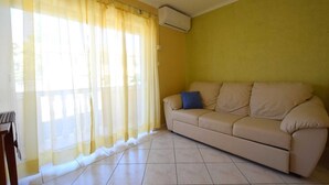 A living room with a beige sofa, yellow curtains, and an air conditioning unit on the wall.
