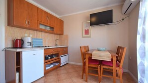 A compact kitchen with wooden cabinets, a small refrigerator, and a dining table with chairs. - Apartment Jelica 4 on the first floor (Njivice)