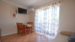 A dining area with a table and chairs, a flat-screen TV mounted on the wall, and a window with patterned curtains. - Apartment Jelica 4 on the first floor (Njivice)