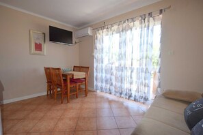 Cozy living space with a dining area and seating area, featuring a flat-screen TV and a window with patterned curtains.