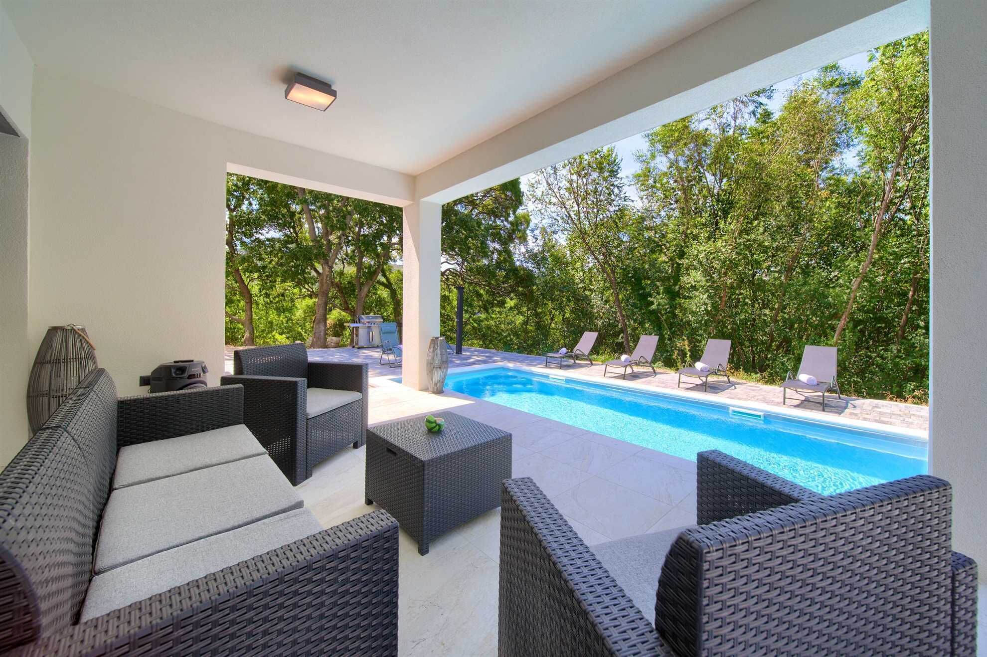 Ein überdachter Außenbereich mit Pool, Liegestühlen und Korbmöbeln.