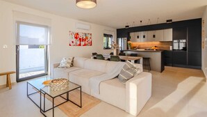 Ein modernes Wohnzimmer mit einer Couch, einem Glastisch und einer Küchenzeile mit Esstisch und Stühlen.