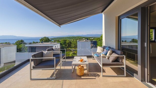 Un espace de vie extérieur moderne comprenant une terrasse, deux canapés, une table basse et une grande fenêtre offrant une vue panoramique.