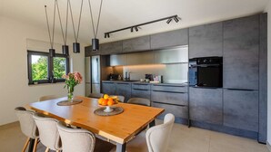 Une cuisine moderne avec des meubles de couleur sombre, une table à manger en bois et un four encastré.