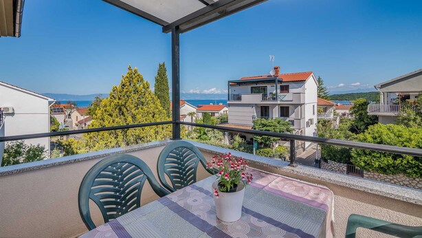 A balcony with a table and chairs, a potted plant, and a view of buildings and trees. - Apartment Katja 3 with sea view (Njivice)