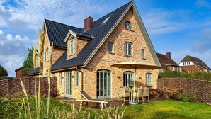 Een groot, wit gevelsteen huis met een schuin dak, een terras met tuinmeubilair en een stenen muur.