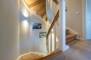 Un escalier avec des marches en bois et des rampes blanches, deux tableaux encadrés accrochés au mur et un interrupteur sur le mur.