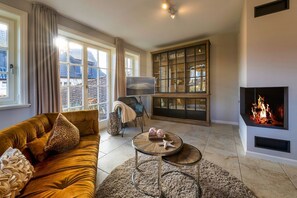 Un salon avec un canapé, une table basse, une cheminée et une grande fenêtre avec des rideaux.