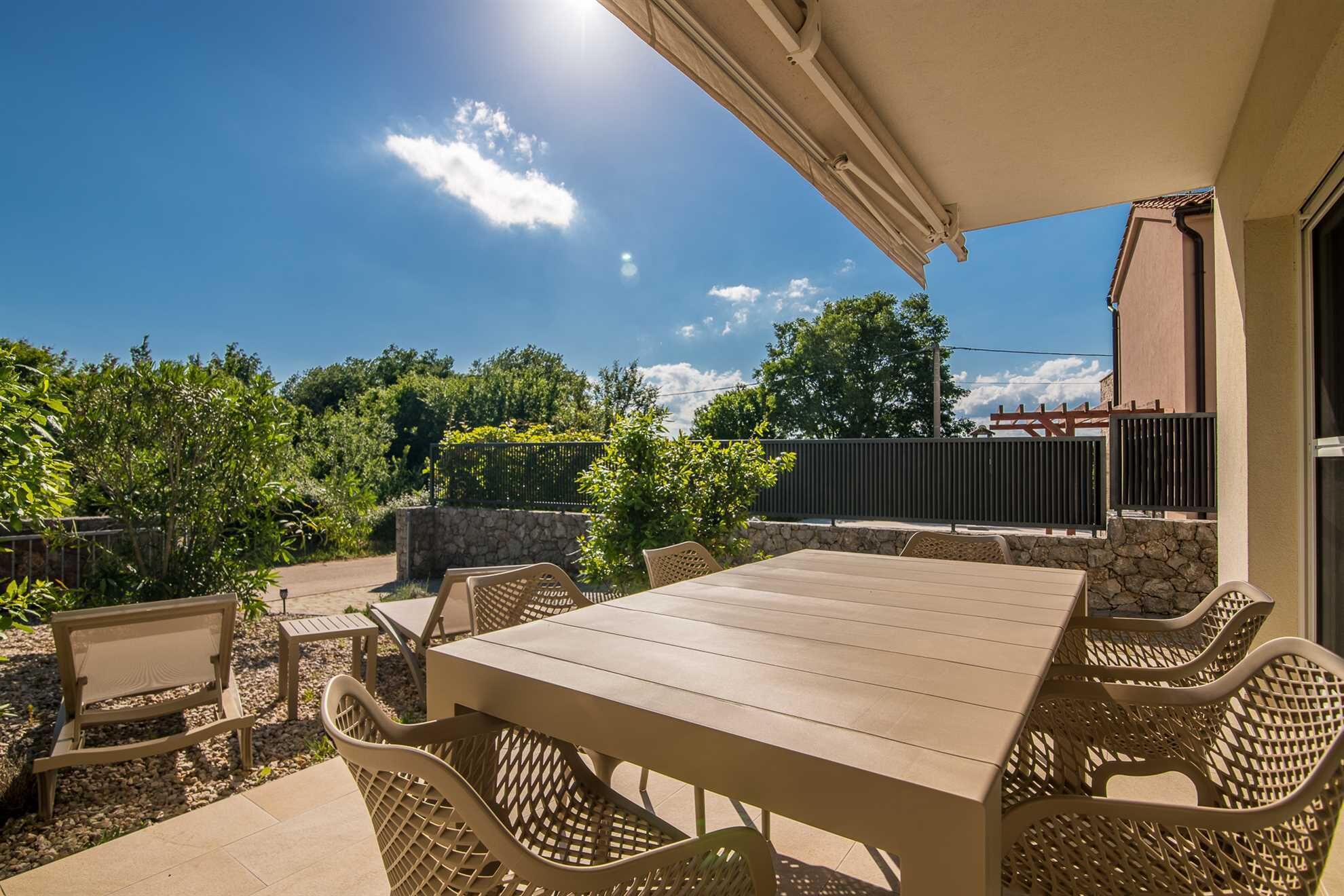 An outdoor patio with a table and chairs, surrounded by greenery and a stone wall.