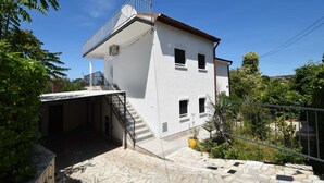 Un edificio de dos pisos con un balcón, una escalera que conduce a la entrada y un camino de entrada pavimentado.