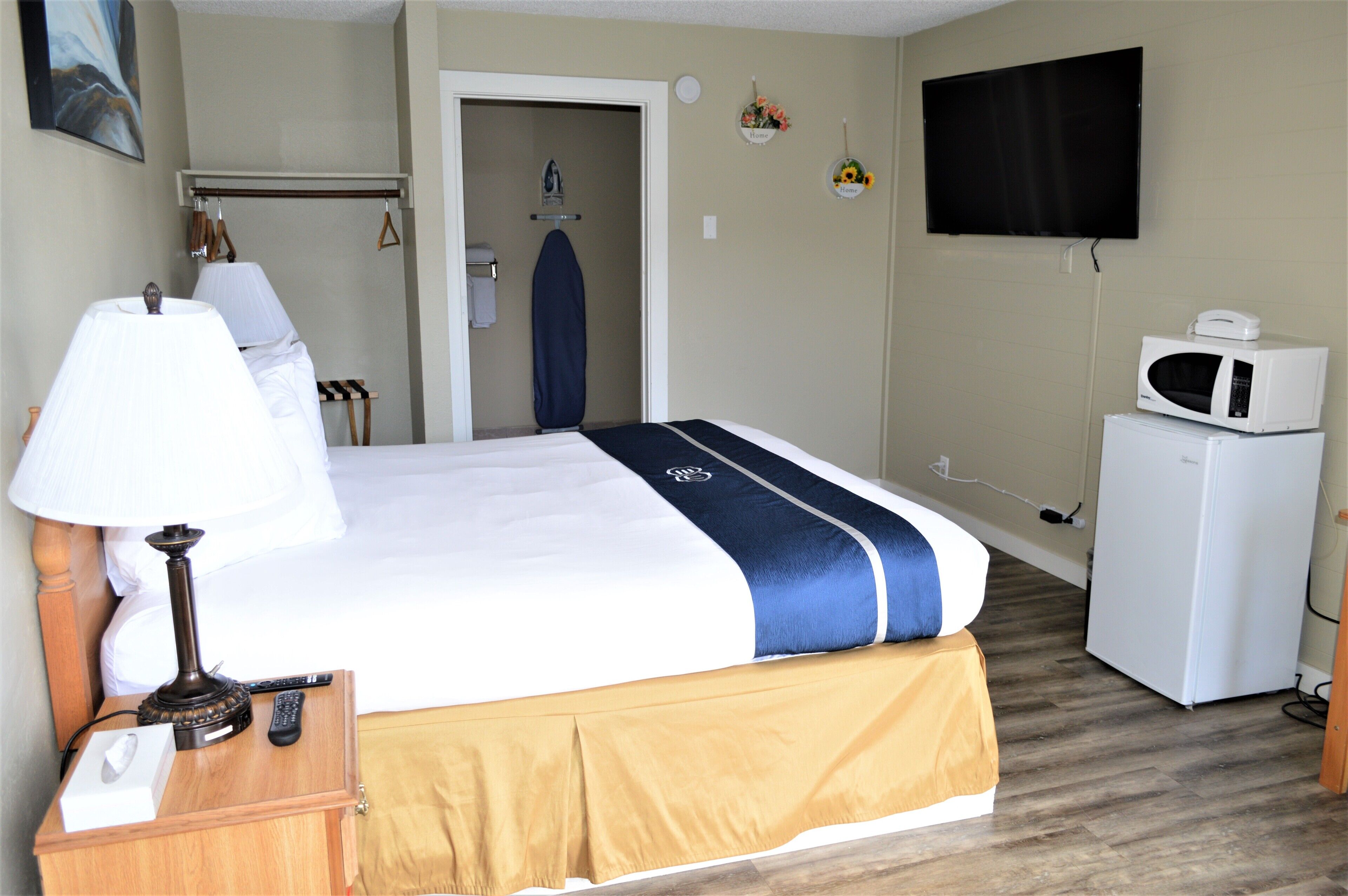 A hotel room with a bed, a bedside table with a lamp, a TV, a microwave, and a door leading to a bathroom.