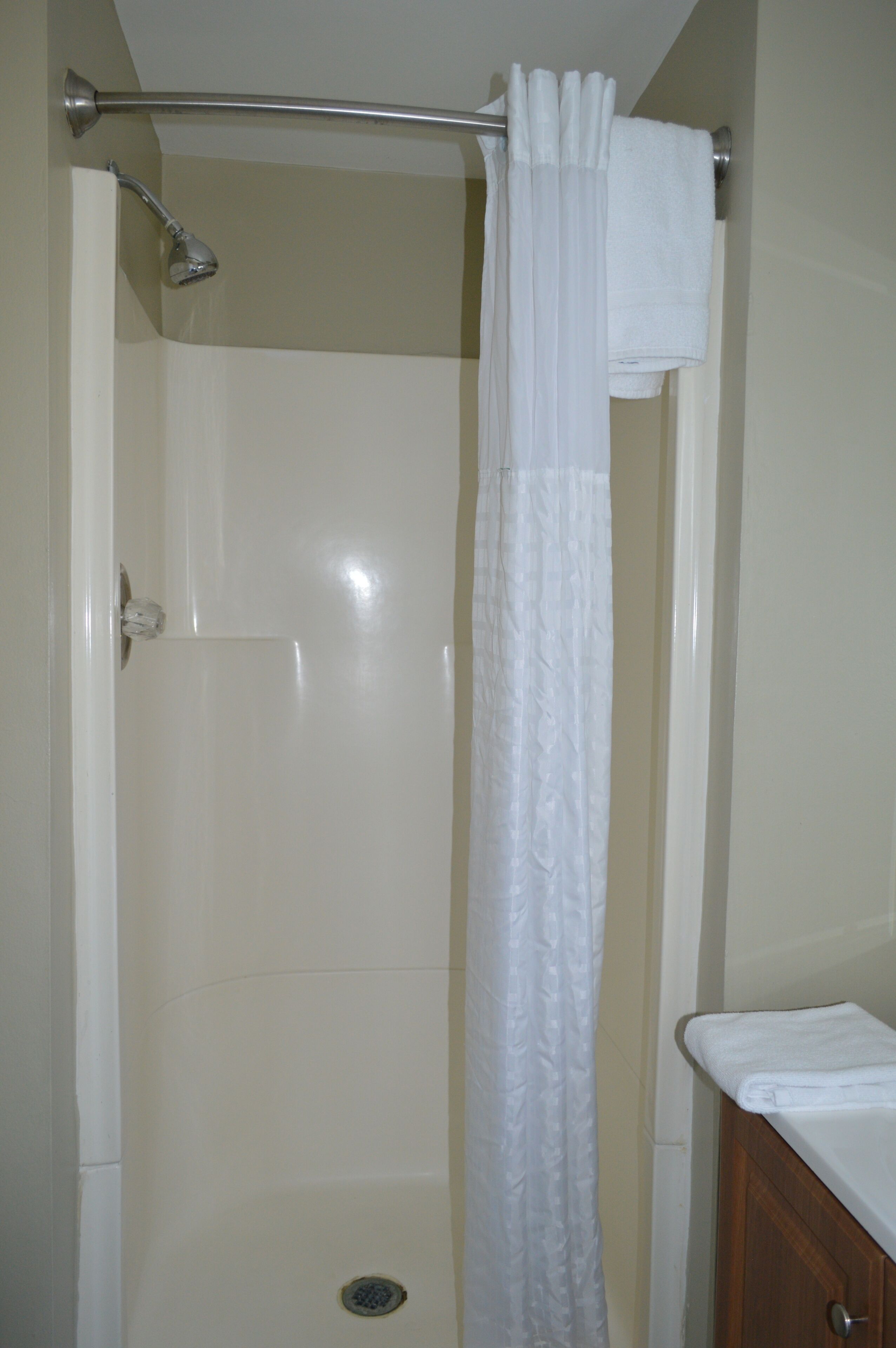 Un baño con ducha, cortina blanca y un mueble de madera.