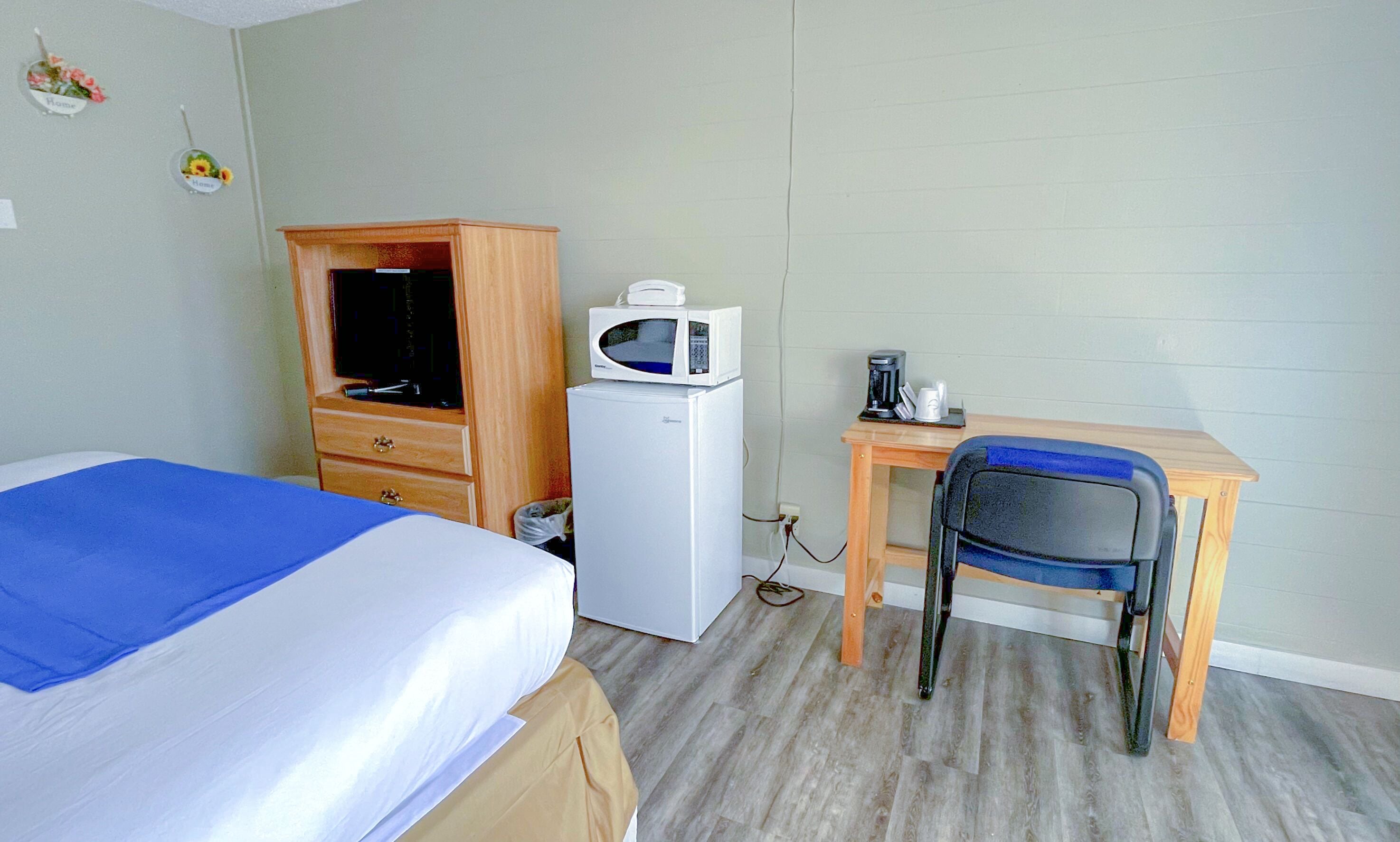 A room with a bed, a desk with a chair, a microwave, and a refrigerator.