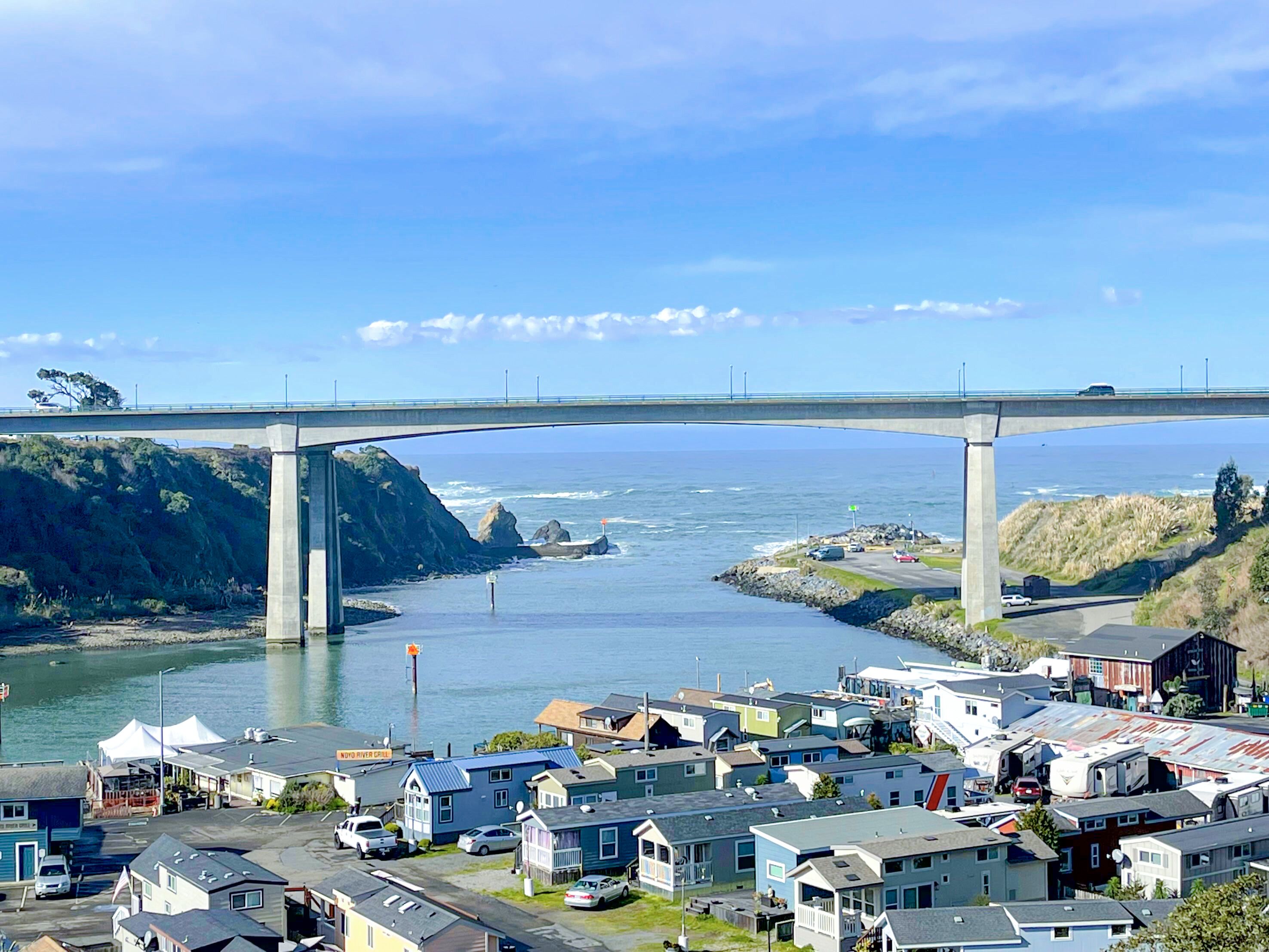 Une ville côtière avec un pont enjambant une rivière, des maisons et un petit port.