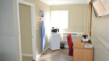 Habitación de hotel pequeña con kitchenette, microondas, refrigerador compacto, escritorio con teléfono y ventana que proporciona luz natural.