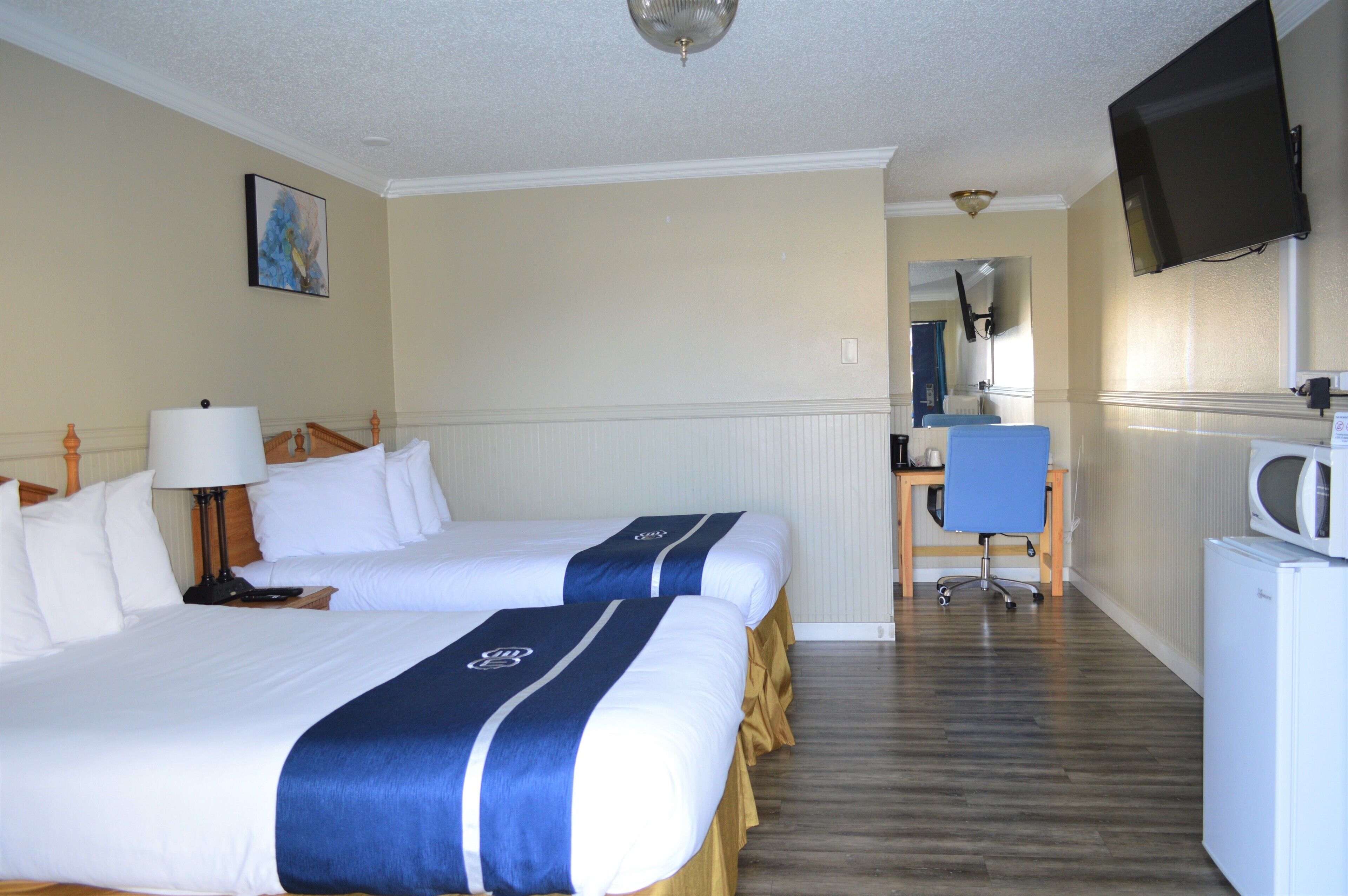 Une chambre d’hôtel avec deux lits, un bureau, une chaise, une télévision et un four à micro-ondes.