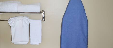 Un baño con un toallero que sostiene dos toallas blancas, una tabla de planchar azul y un planchador en la pared.