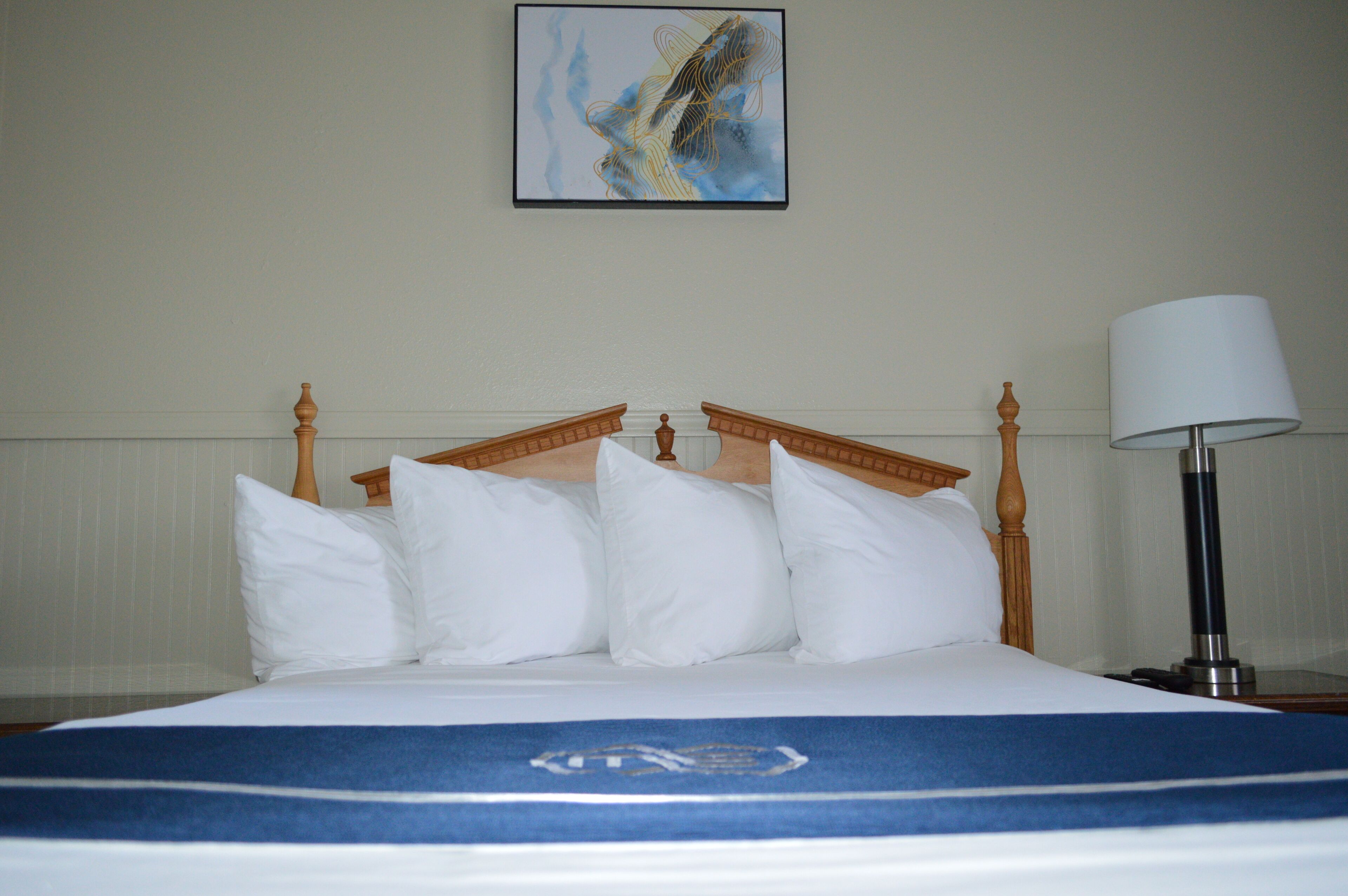 A hotel room with a bed, pillows, a lamp, and a painting on the wall.