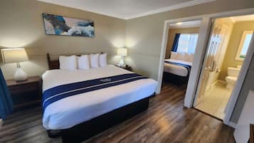 Ein Hotelzimmer mit einem großen Bett, einem Nachttisch, einer Lampe, einem Bild an der Wand und einem durchgegangenen Tür erkennbaren Badezimmer.