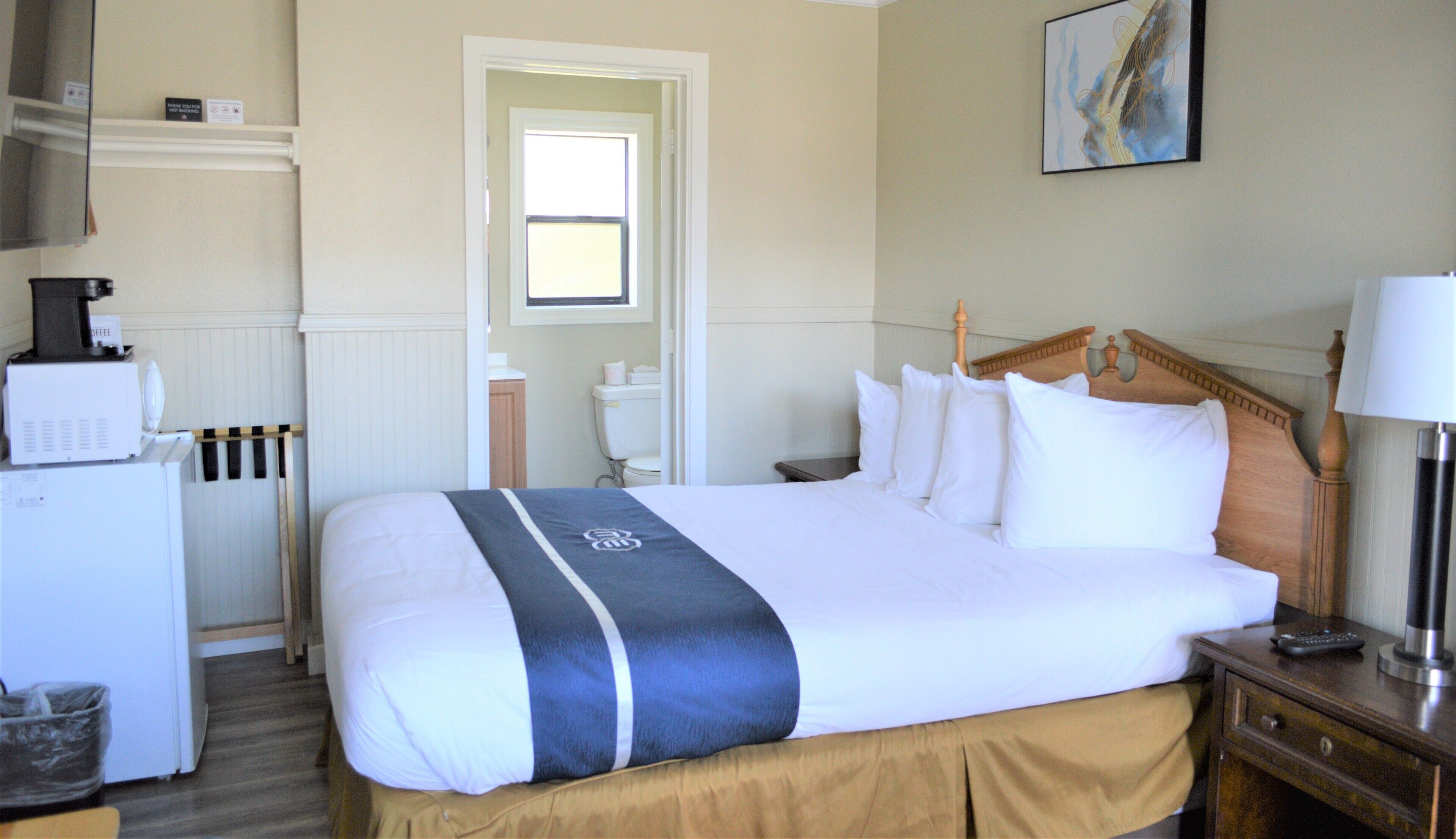 A hotel room with a bed, a bedside table with a lamp, a coffee machine, and a view of the hallway.