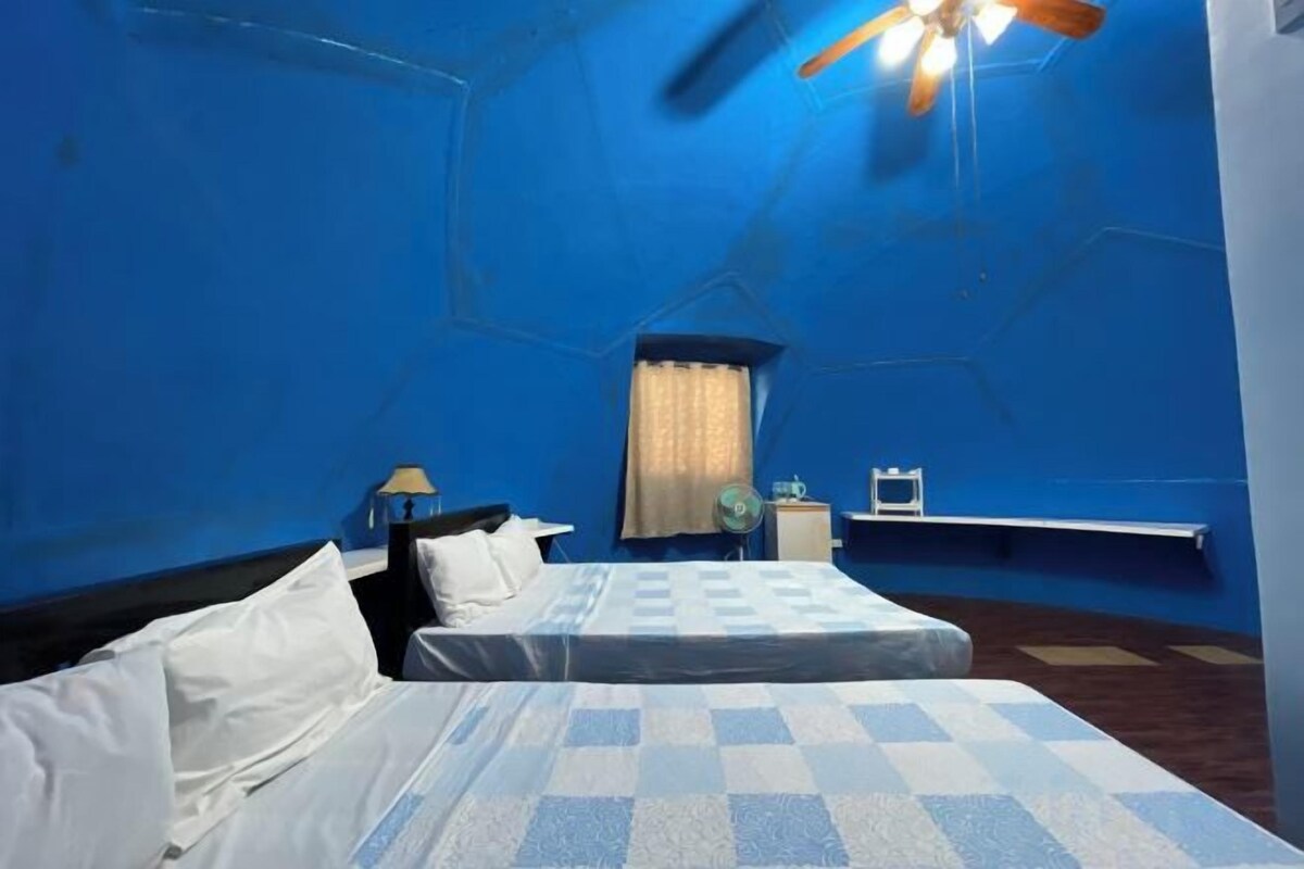 Une chambre avec deux lits, un bureau, une chaise, une fenêtre avec des rideaux et un ventilateur de plafond.