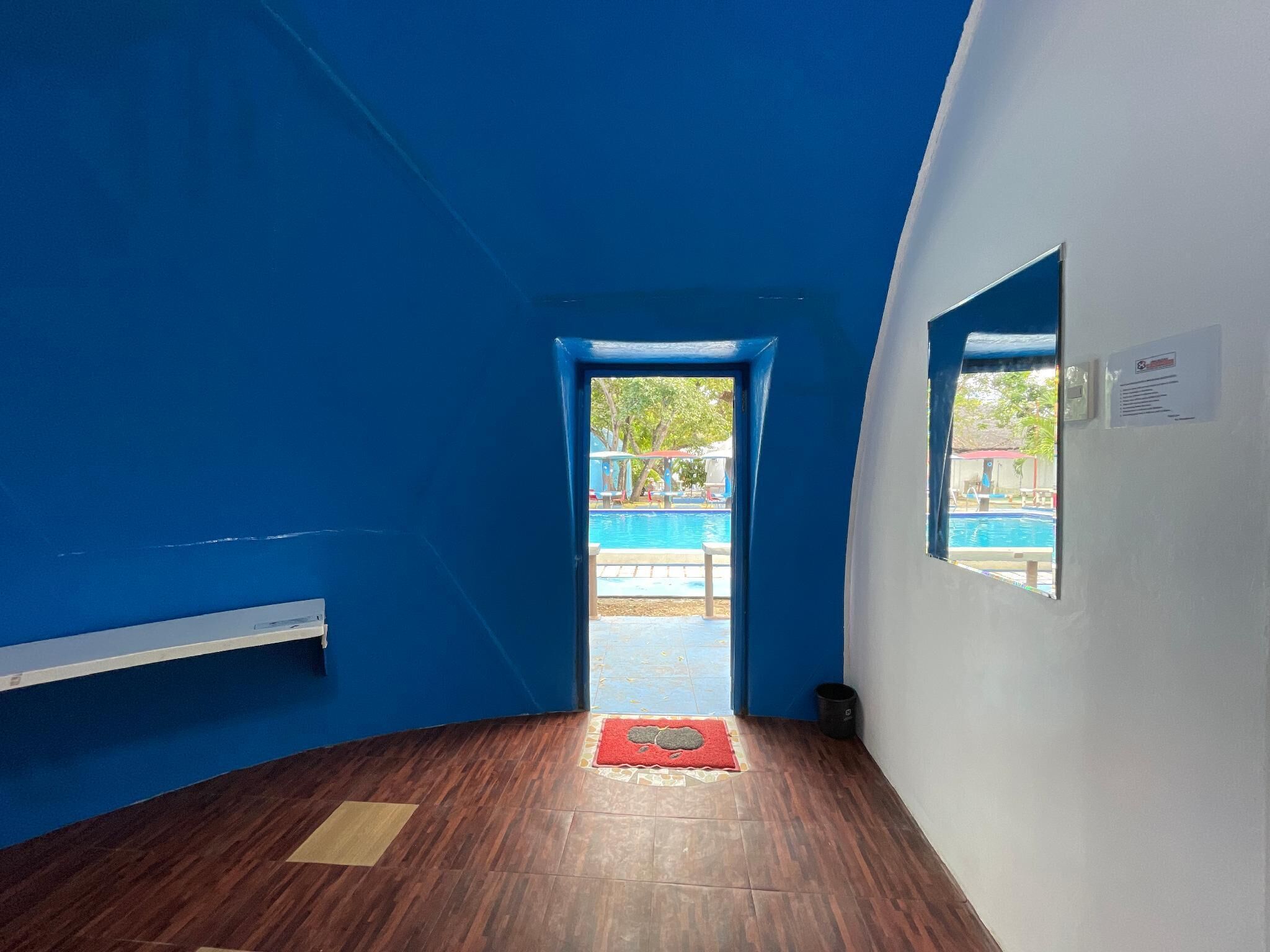 Una habitación con piso de madera, un felpudo rojo en la entrada, una ventana y una puerta que da al exterior.