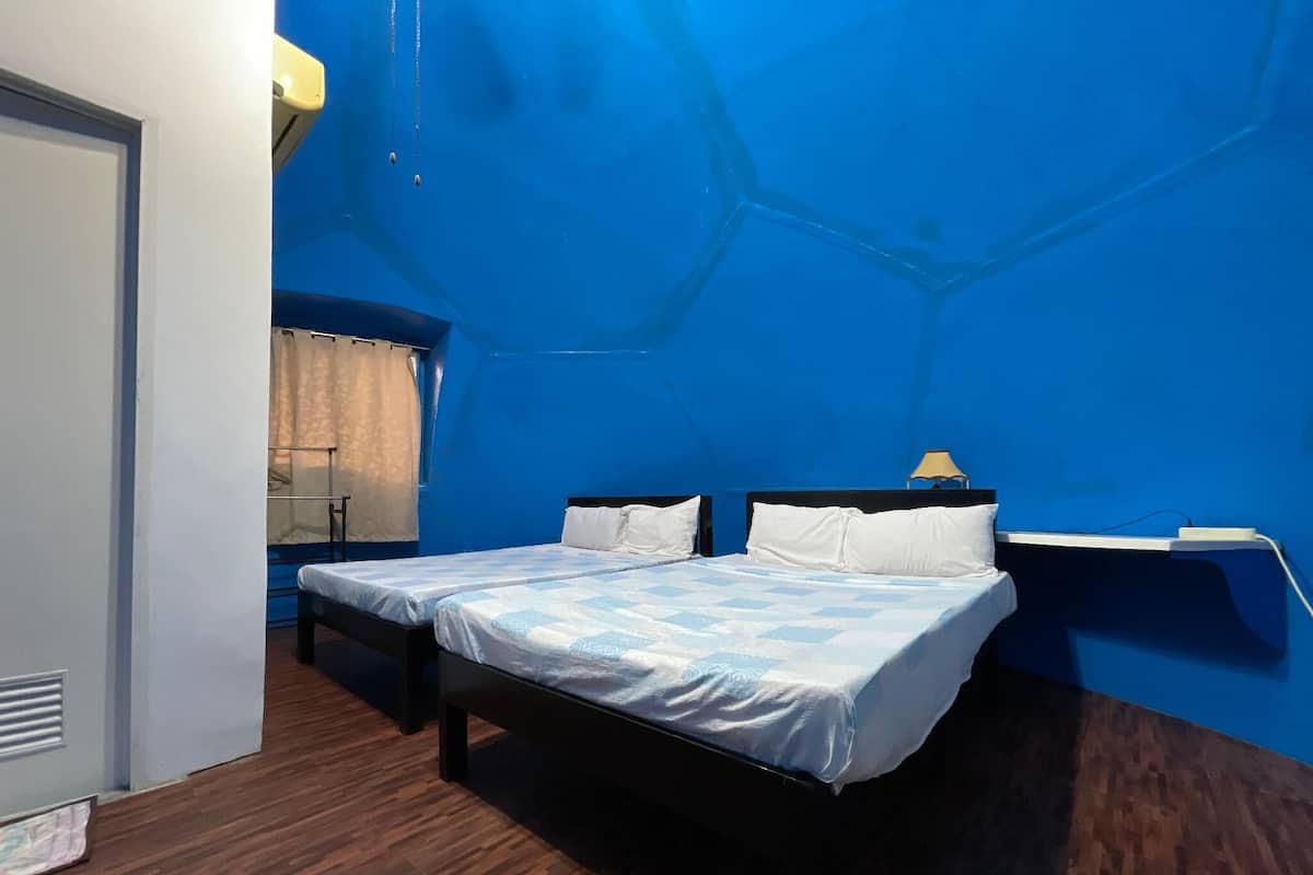 Een kamer met twee bedden, een houten vloer, een blauwe muur en een raam met gordijnen.