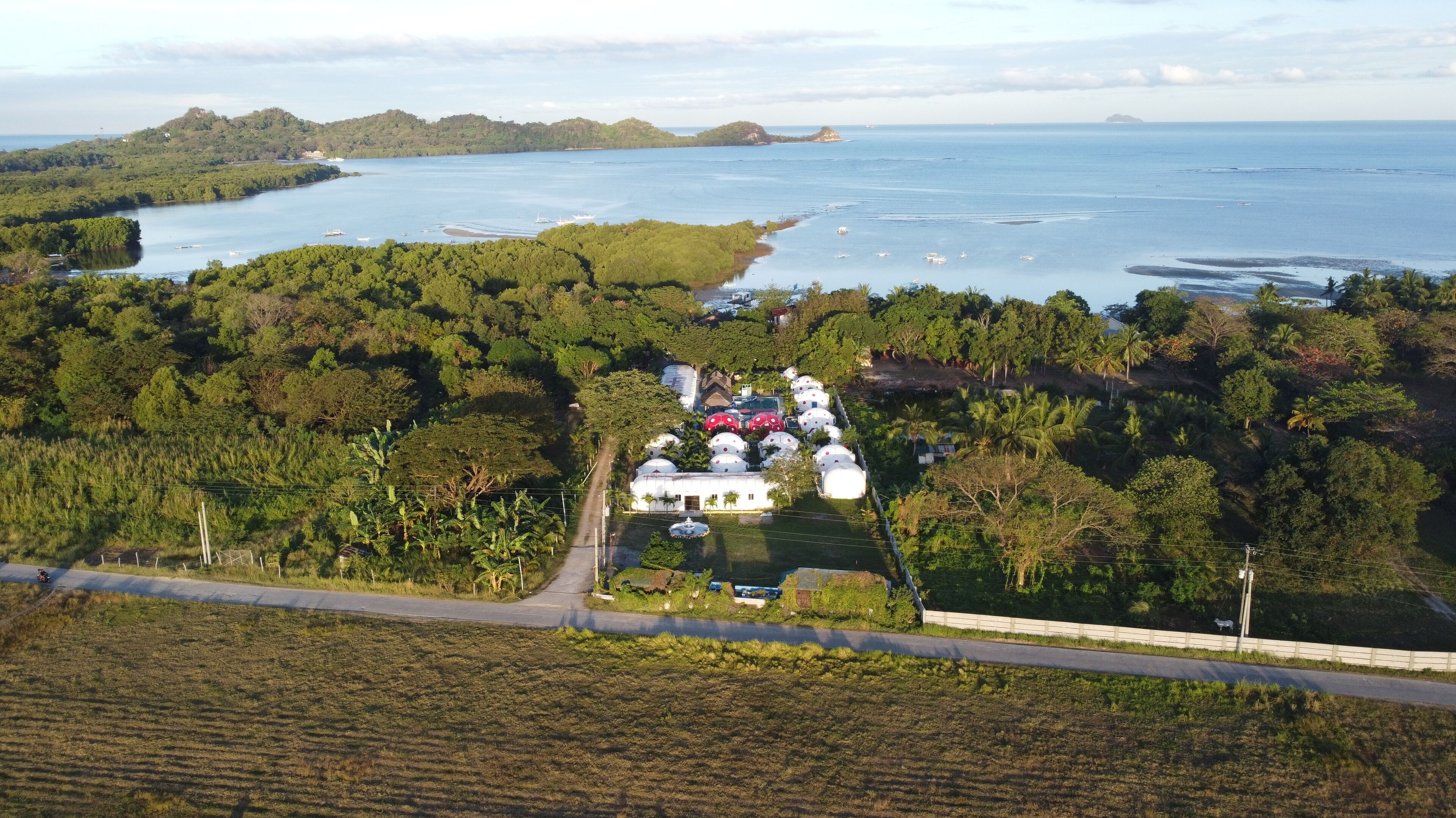An aerial view of a coastal area with a cluster of dome-shaped buildings surrounded by lush greenery and a body of water.