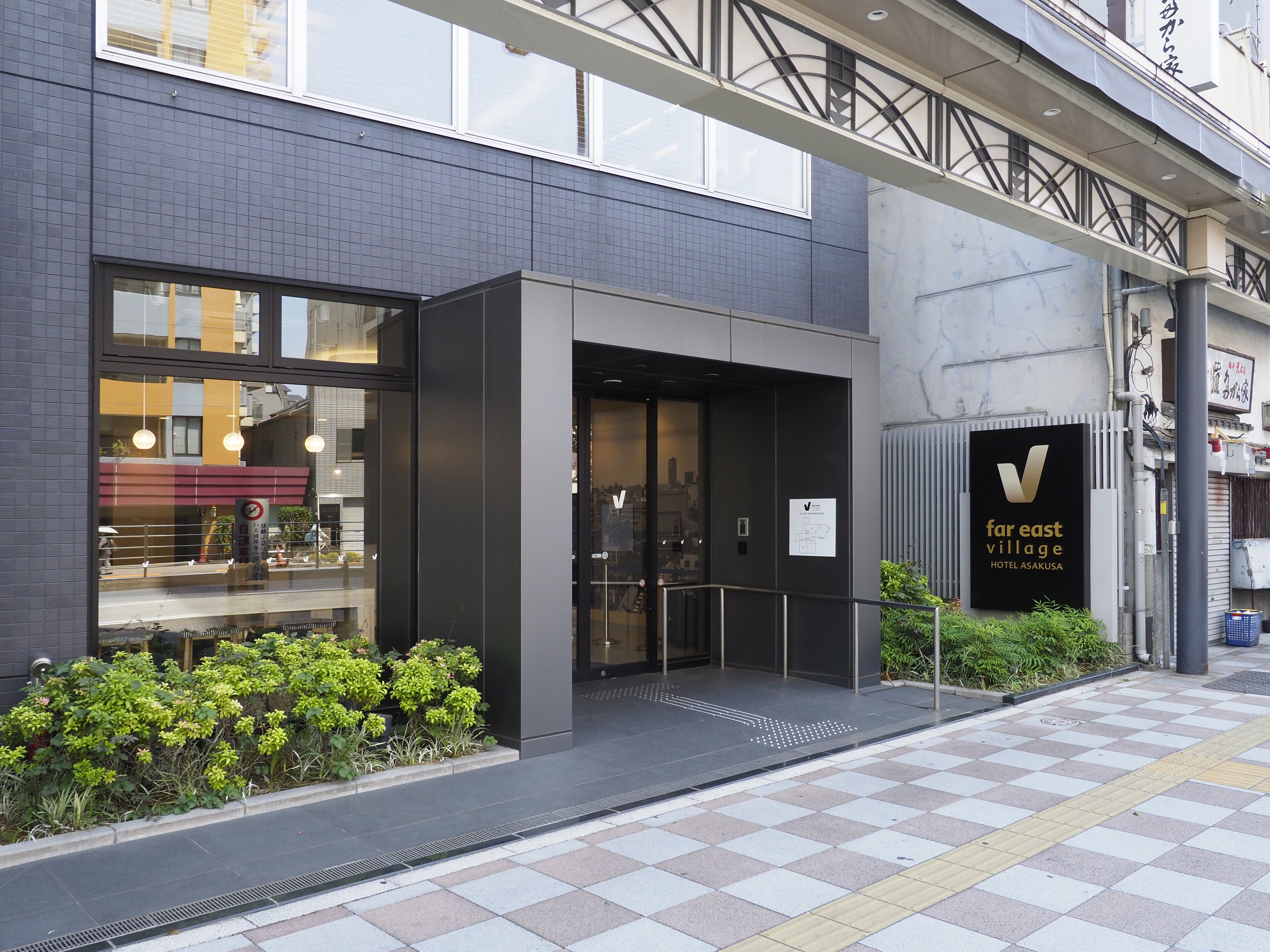 A hotel entrance with a modern design, a visible entrance door, and a signboard for 'Far East Village Hotel Asakusa'.