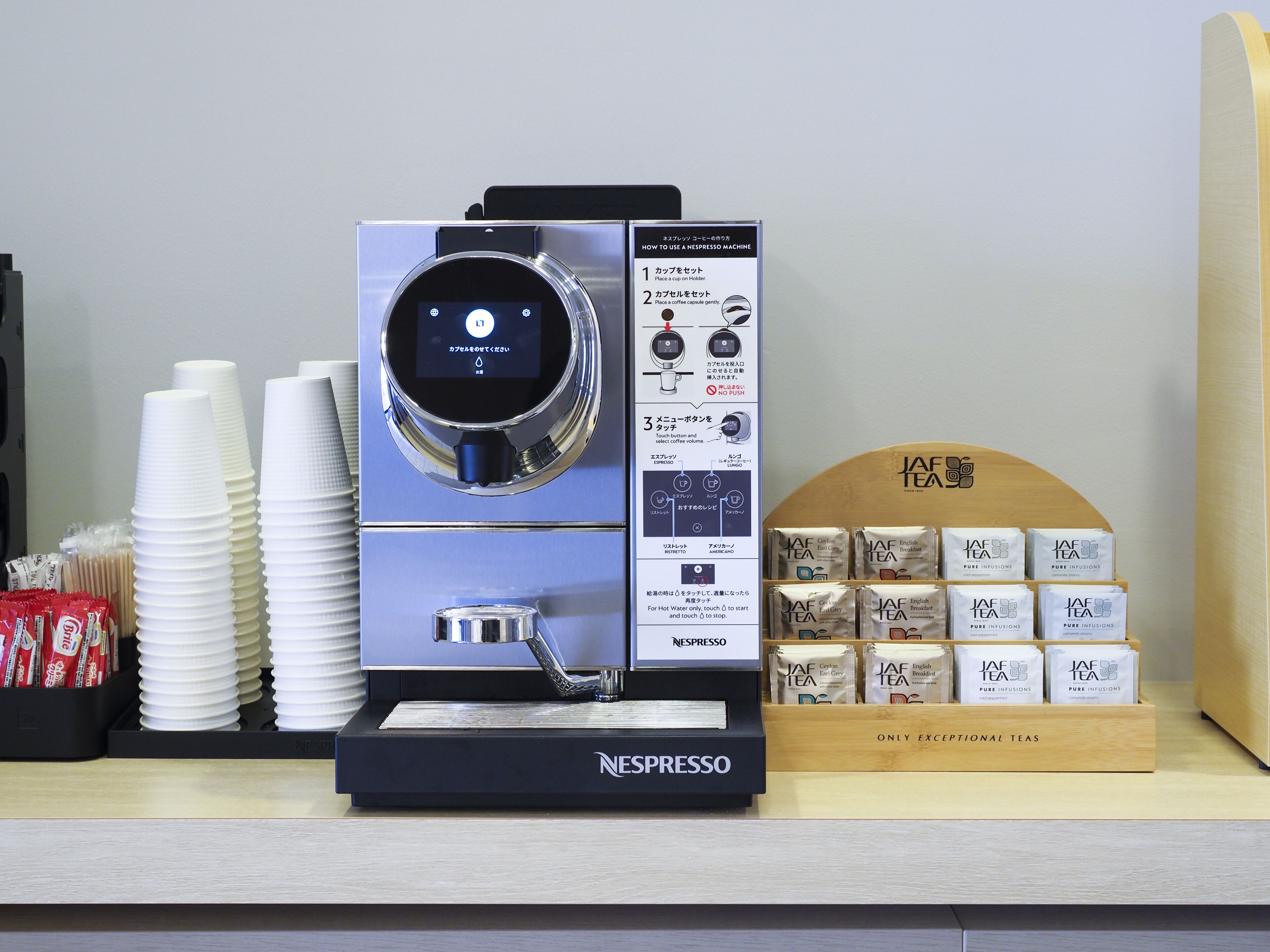 A Nespresso coffee machine with instructions, disposable cups, and a display of tea bags.