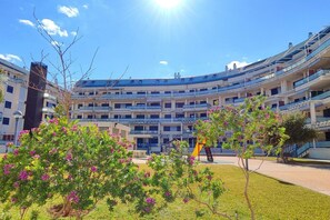 A multi-story building with balconies, a playground, and a clear sky.