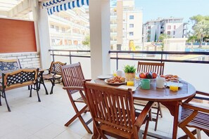 A balcony with a table set for breakfast, wooden chairs, and a view of the cityscape.