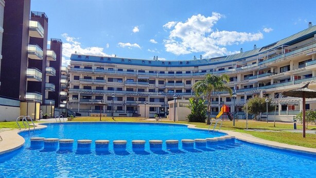 En swimmingpool omgivet af et hotel med flere etager, altaner og en legeplads.