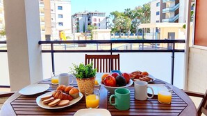 En balkon med morgenmadsprodukter, en grøn kop og en skål med frugt.