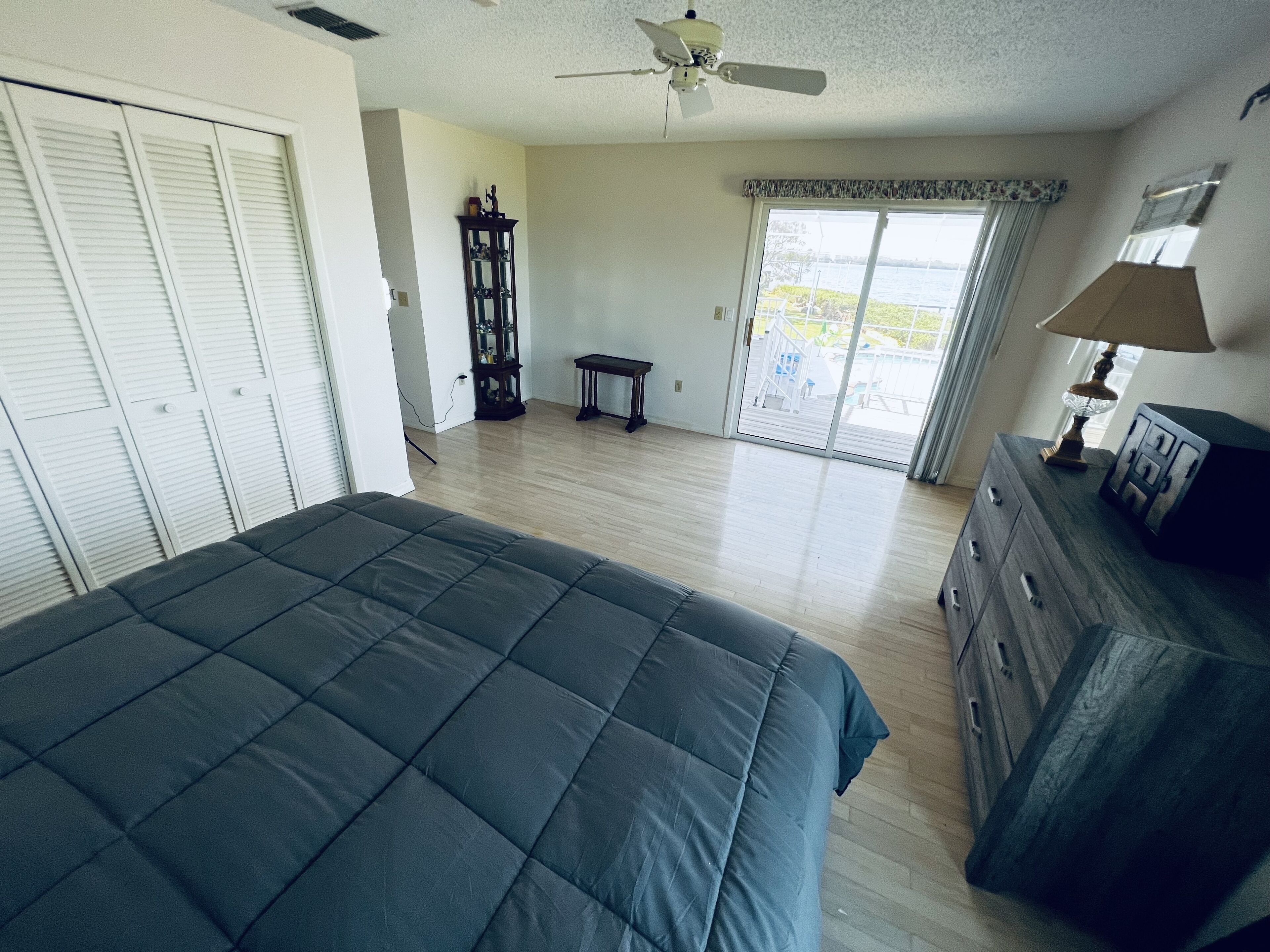 A bedroom with a bed, a dresser, a ceiling fan, and a view through a window.