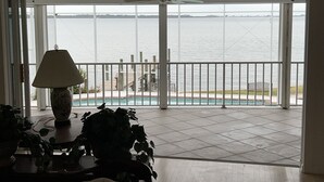 A room with a view of a body of water, a balcony with a railing, and a table with a lamp and plants. - The Bays Edge Retreat Waterfront (Bradenton)
