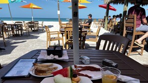 A beachside restaurant with outdoor seating, a menu, and a variety of breakfast items including eggs, toast, and fruit. - The Bays Edge Retreat Waterfront (Bradenton)