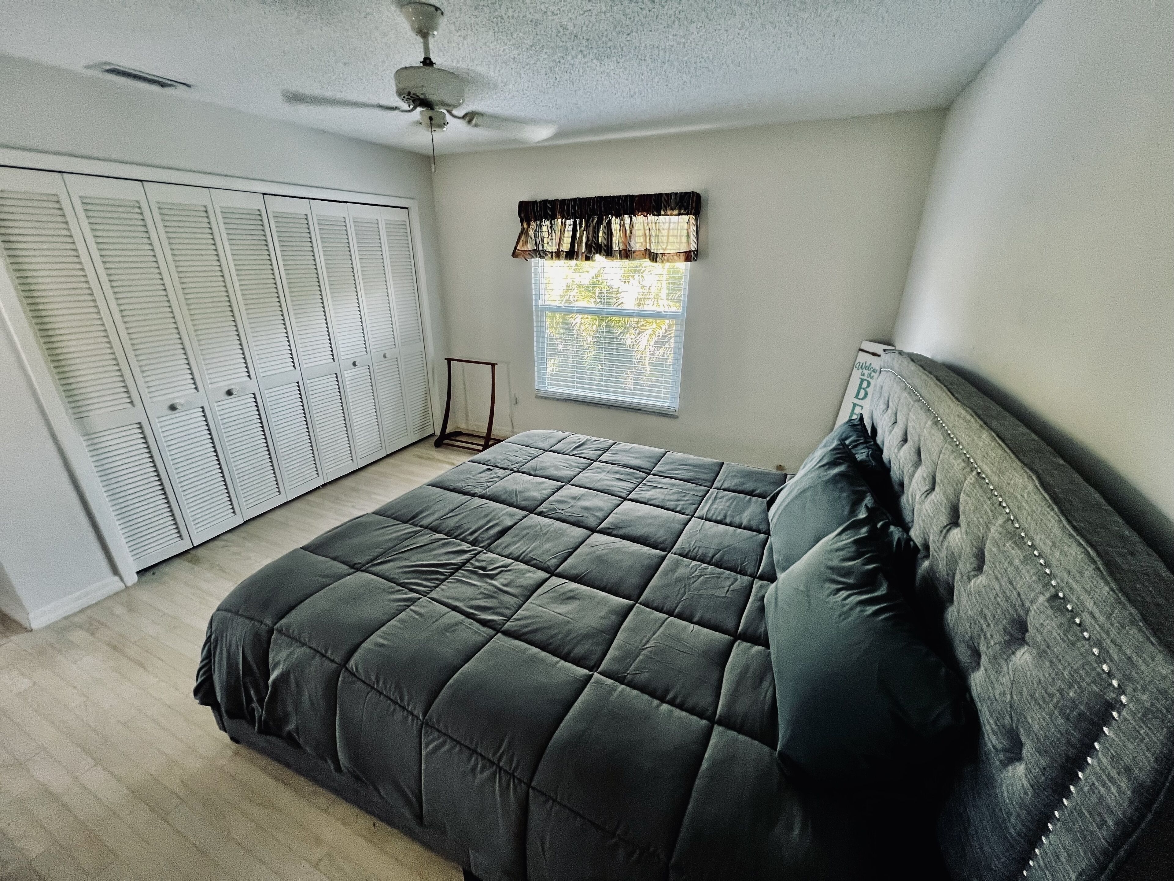 Een slaapkamer met een bed, een plafondventilator, een raam met zonwering en een kledingkast met verstelbare deuren.