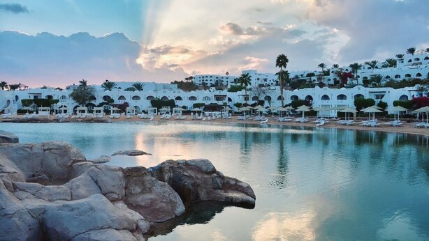 A resort with white buildings, a pool, and a rocky shoreline. - Domina Coral Bay Sultan - Private room (Sharm el Sheikh)