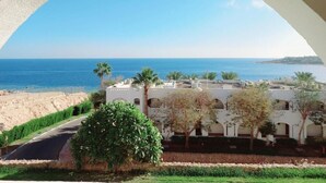A view through an arched window overlooking a beach, a white building with arches, and a clear blue sky. - Domina Coral Bay Sultan - Private room (Sharm el Sheikh)