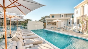 A pool area with lounge chairs and umbrellas, a bar, and a building with a stone facade.