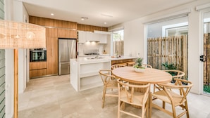 A modern kitchen with white cabinets, a stainless steel refrigerator, and a wooden dining table with wicker chairs.