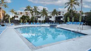A swimming pool with blue lounge chairs and palm trees, surrounded by modern buildings.