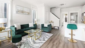 A modern living room with a green sofa, a glass coffee table, and a bar stool. - Inspiration at The Cove Riverwalk Villas (Wilmington)